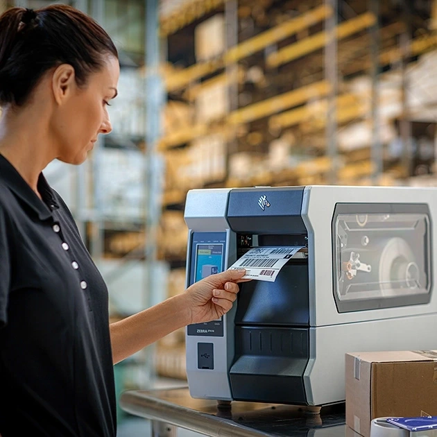 Opératrice utilisant une imprimante code-barres industrielle pour imprimer des étiquettes en entrepôt logistique